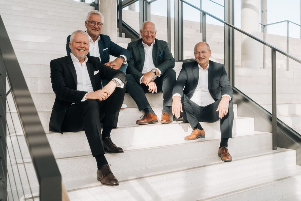 Die vier Gründer - Hans-Jürgen Lang, Eric Günther, Udo Junglen, Eckhard Dehning - der heads4success GmbH sitzend auf einer Treppe.